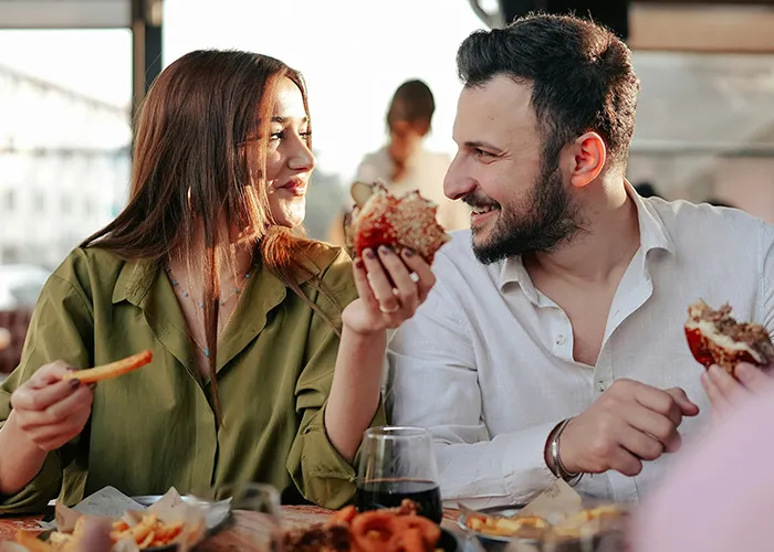 Young man and woman sharing food and laughing together, enjoying a casual meal with savage insults conversation.