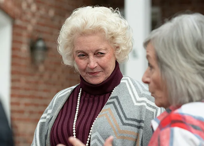 Two older women engaged in a conversation with witty expressions, illustrating savage insults in a casual setting.