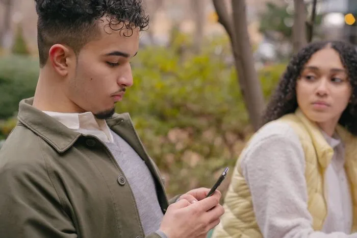 Young man distracted by phone while woman looks on, illustrating what makes a man instantly unattractive to women.