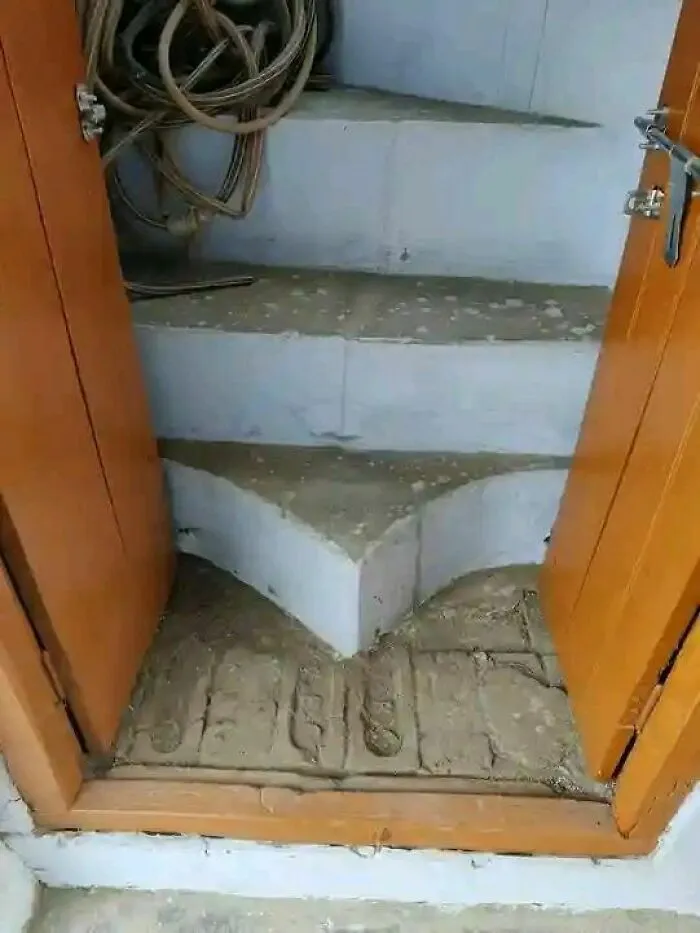 Narrow and uneven stairs with improper landing area inside a small wooden door, showcasing engineering mistakes.