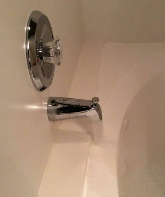 Bathtub faucet installed too far from tub edge, showing a hilariously dumb engineering mistake in plumbing setup.