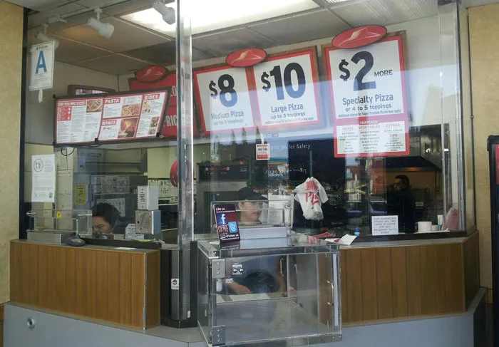 Pizza shop counter with plastic safety barrier, illustrating signs to look out for to avoid unsafe neighborhoods and areas.