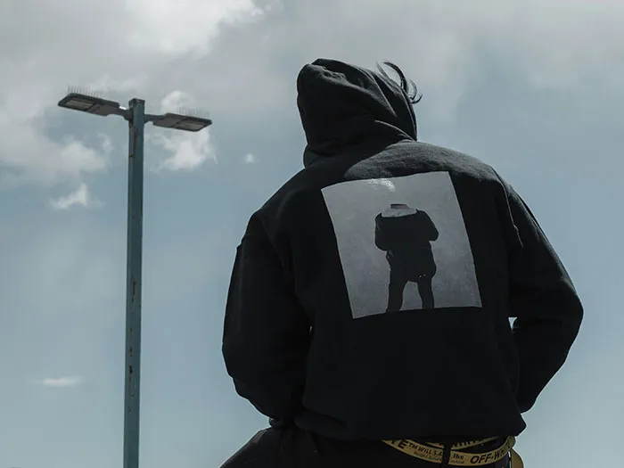 Person in dark hoodie sitting near a streetlight under cloudy sky, illustrating signs to look out for unsafe neighborhoods.