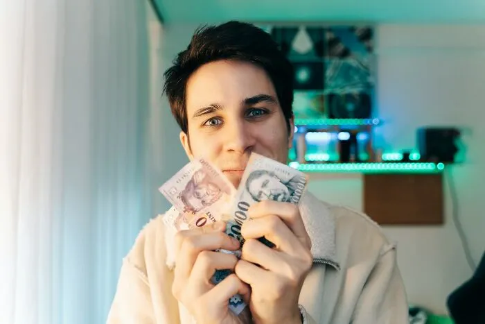 Young man holding money close to his face, illustrating traits that make a man instantly unattractive to women.