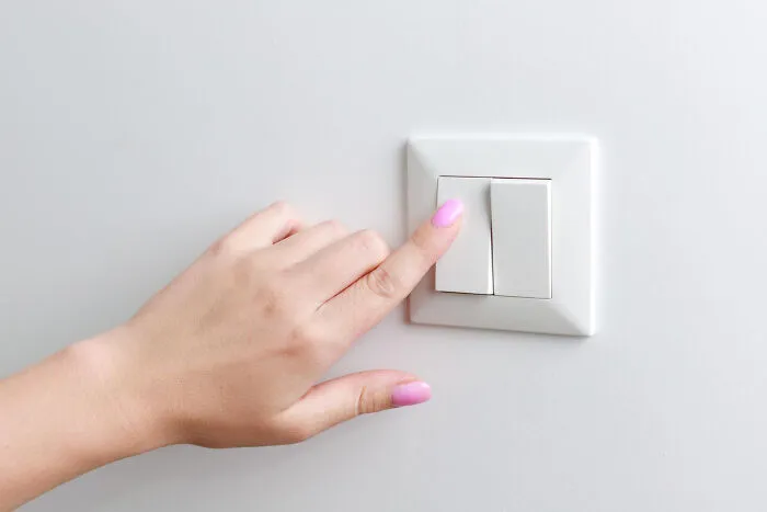 Hand with pink nails pressing a light switch on a white wall symbolizing smooth pickup lines and interaction.