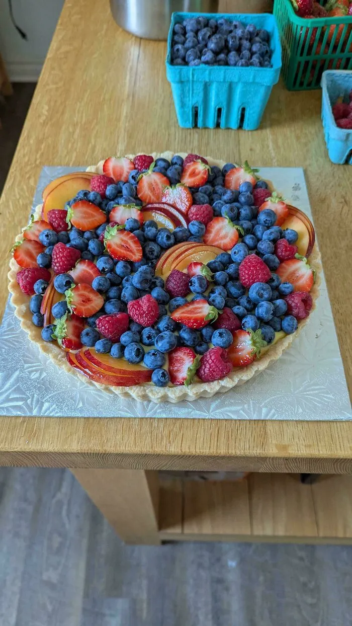 Fruit tart topped with fresh blueberries, strawberries, raspberries, and sliced nectarines showcasing gorgeous baked goods art.
