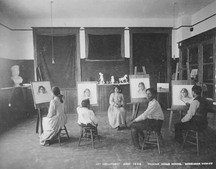 Native American boarding school students in an early 1900s classroom drawing portraits during art class.