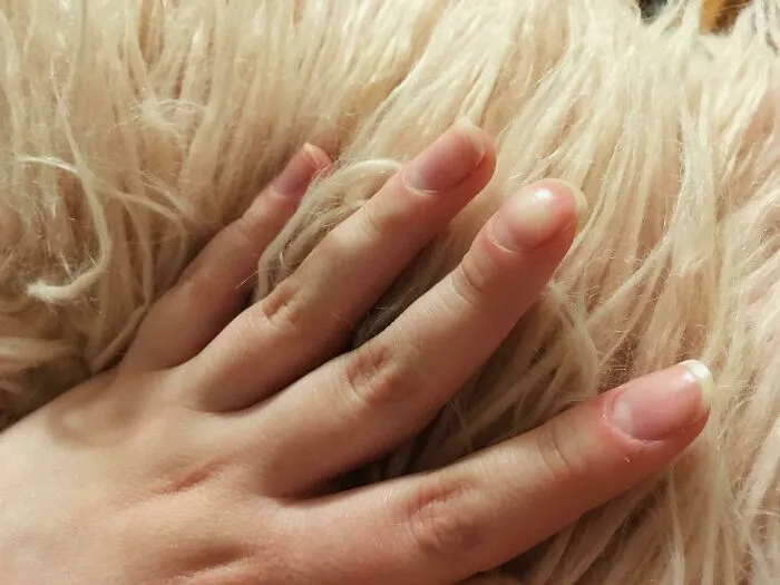 Mano femenina con piel clara y uñas naturales sobre superficie de pelaje suave, destacando rasgos distintivos del cuerpo humano.