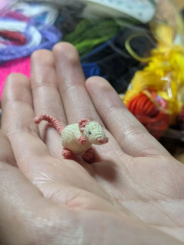 Tiny crochet mouse held in a hand with colorful yarn in the background, showcasing crochet enthusiasts' incredible creations.