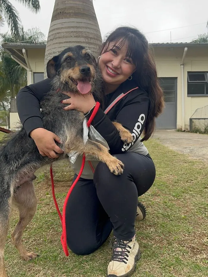Young woman happily hugging a joyful shelter dog on a leash outdoors, capturing the pure joy of shelter dogs.