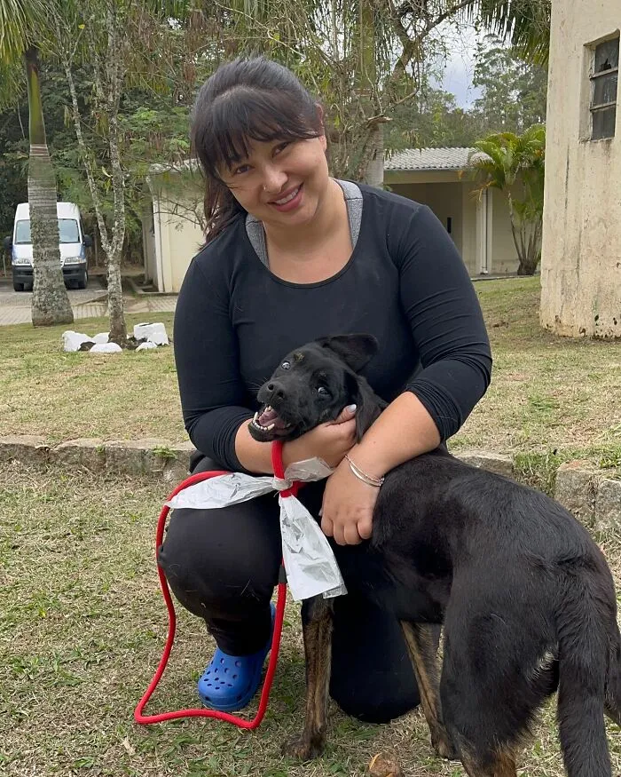 Woman smiling and hugging a joyful shelter dog on a grassy area during one of their weekly walks.