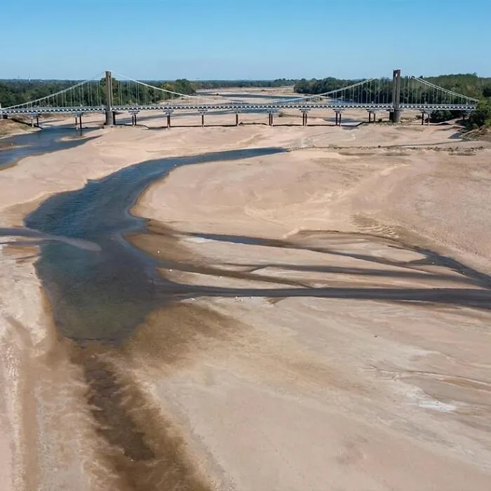 A largely dried-up riverbed with a suspension bridge crossing over it, showcasing an interesting natural scene.