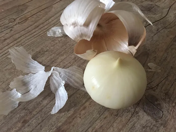 Peeled garlic bulb with papery skin on a wooden surface, featured in interesting online community posts.