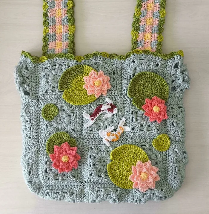 Crochet bag with floral and koi fish design featuring pastel colors, showcasing intricate crochet craftsmanship by enthusiasts.