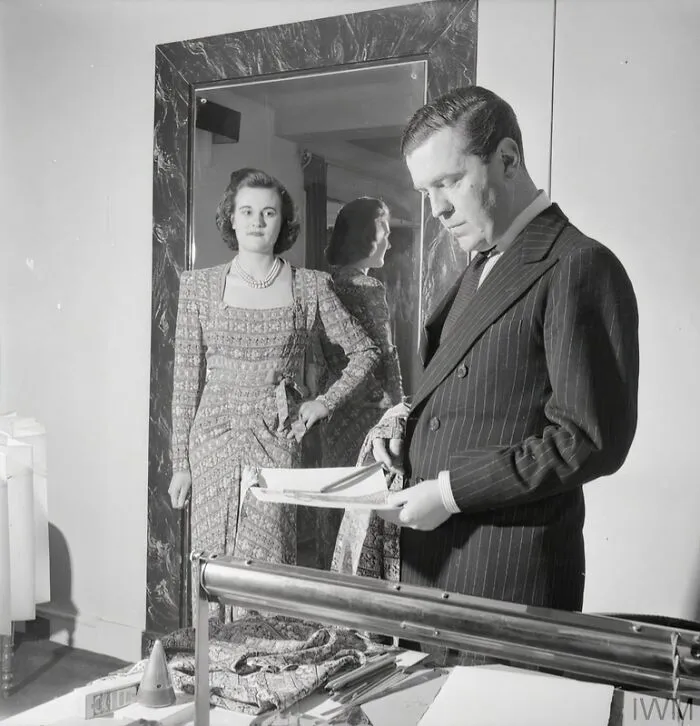 In His London Office, Fashion Designer Norman Hartnell Compares His Original Sketch And Fabric Sample To The Finished Garment, Worn By A Model, Which Has Just Been Completed In His Workrooms