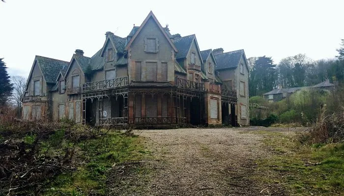 Large abandoned mansion with boarded windows and overgrown surroundings, an eerie example of abandoned places.
