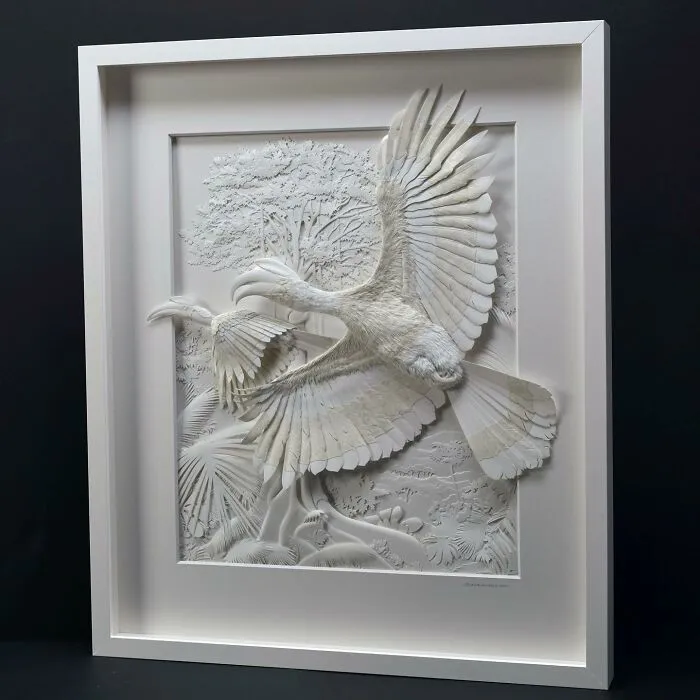 Intricately detailed paper sculpture of realistic wildlife featuring two large birds with outstretched wings in a white frame.