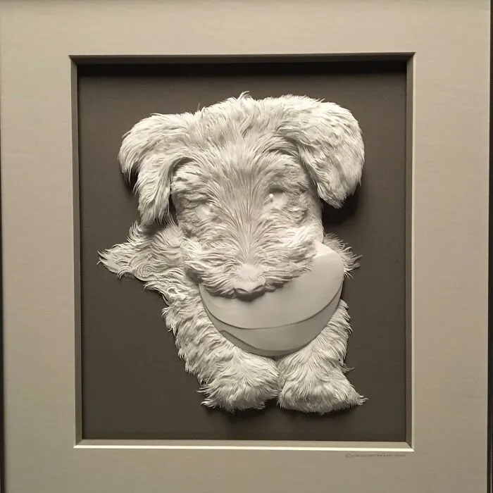Realistic wildlife sculpture of a dog holding a ball, crafted from simple paper with intricate detail and texture.
