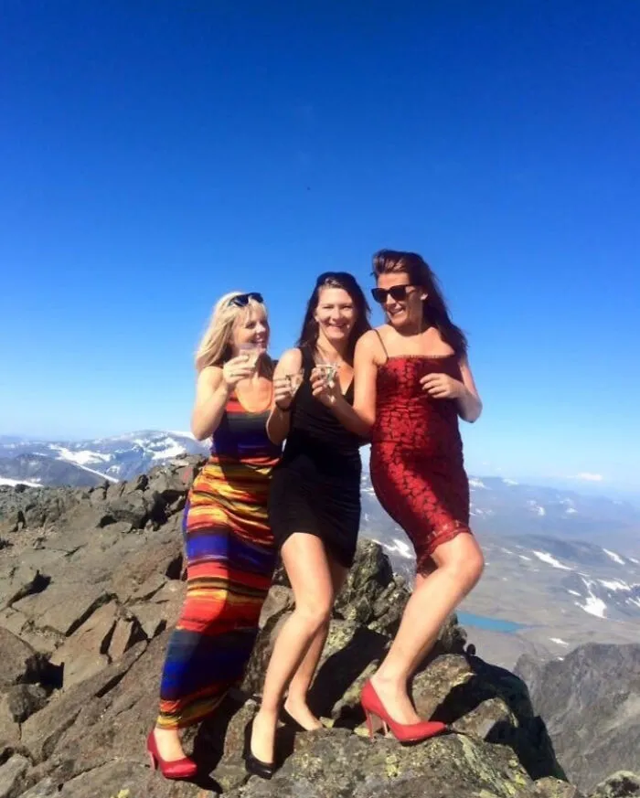 Tres mujeres con vestidos elegantes y tacones en la cima de una montaña disfrutando vacaciones de verano divertidas.