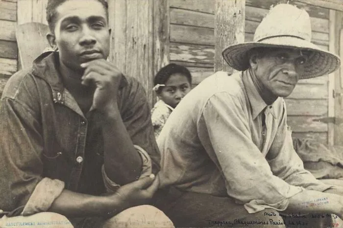 Two men and a child sitting outside a wooden building during the Great Depression, capturing the era's hardship.