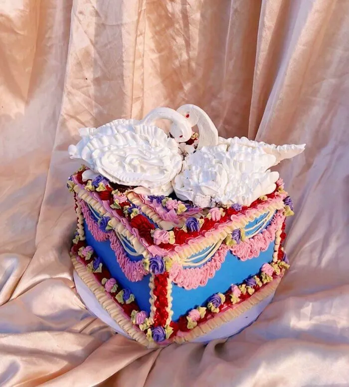 Decorated square cake with intricate piped frosting and meringue swan toppers showcasing gorgeous baked goods artistry.