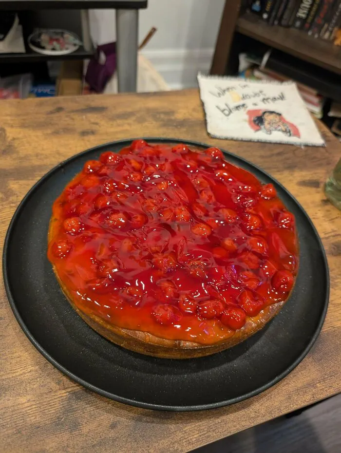Cherry-topped baked goods on a black plate showcasing the glossy, vibrant fruit topping on a rustic wooden table.