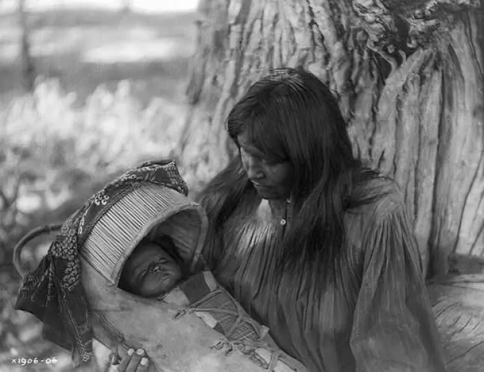 Apache Woman, At Base Of Tree, Holding Infant In Cradleboard In Her Lap, 1906