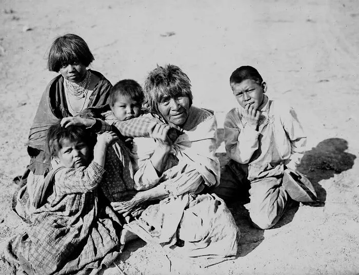 Apache Indian Grandmother Carrying Her Grandchild On Her Back And Three Others Sitting Nearby, Palomas Indian Reservation, 1903
