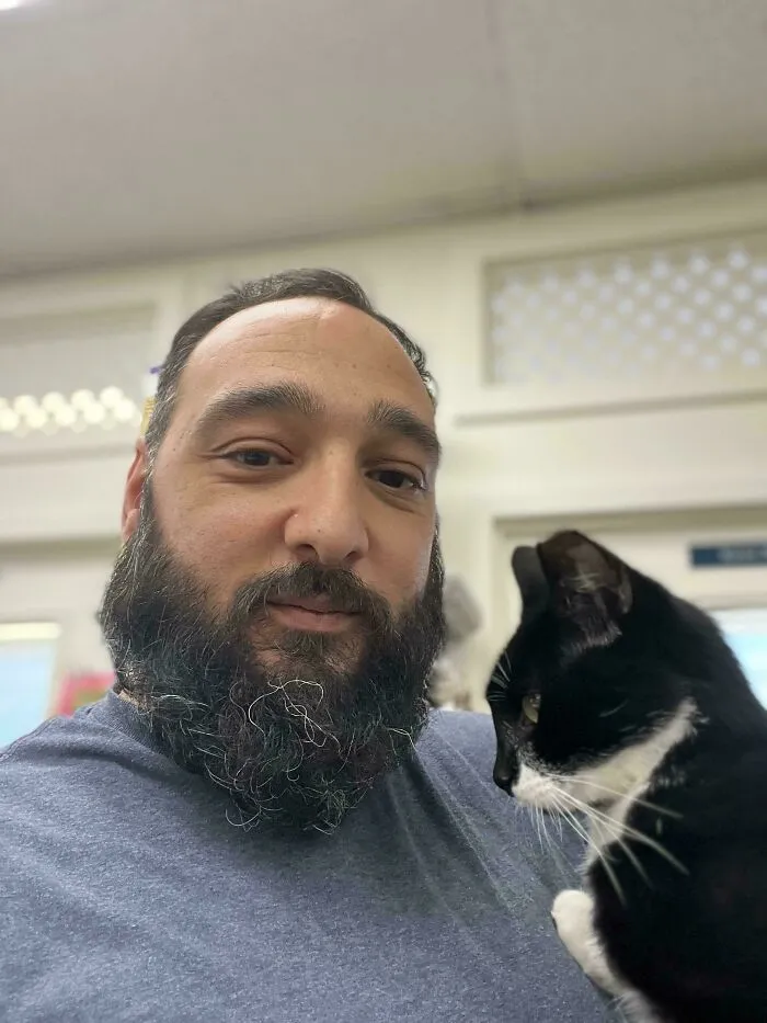 Man with a beard holding a black and white adopted cat, showing love and care for the animal indoors.