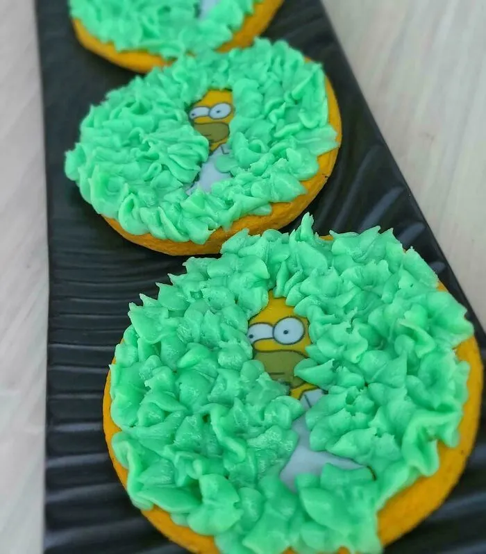 Cookies decorated with green frosting partially revealing ’90s cartoon character images on a black tray, nostalgic ’90s posts theme.