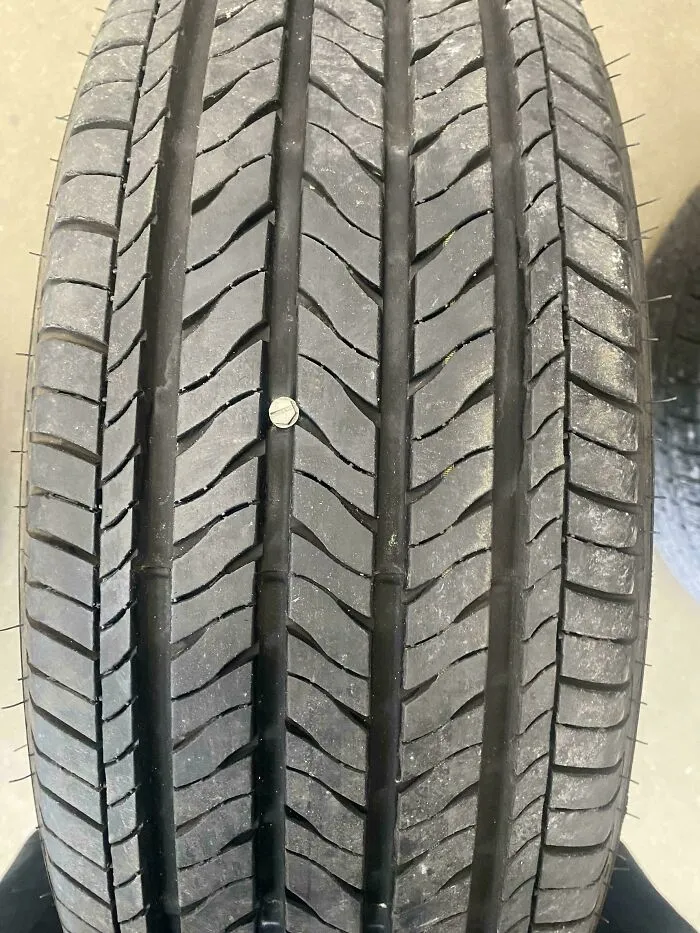 Neumático con un tornillo incrustado, imagen tomada por mecánico para mostrar daño real en reparación de autos.
