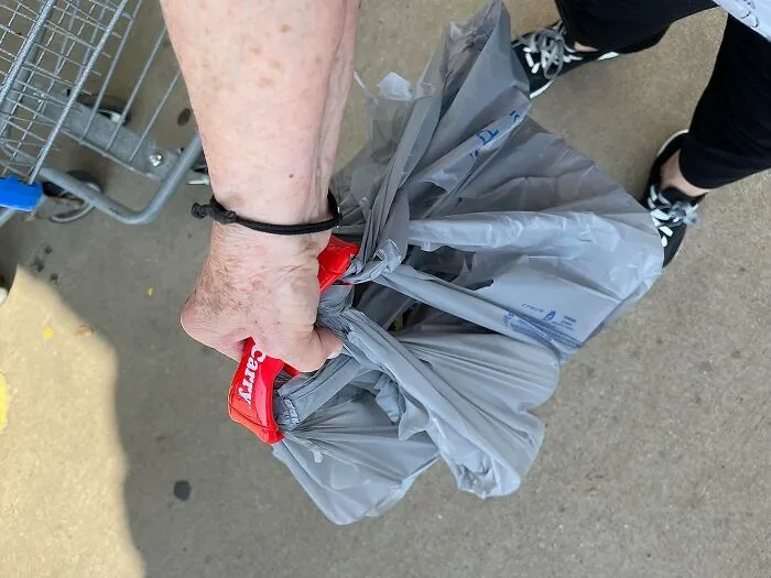 Person holding multiple heavy grocery bags with a red handle, demonstrating durable products for everyday use.