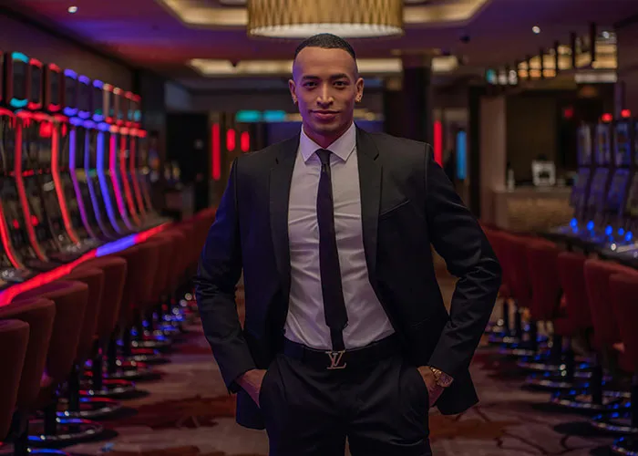 Man in a suit standing confidently in a casino with slot machines, highlighting jobs that only a person without a soul would do