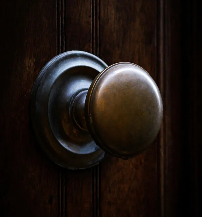 Close-up of a vintage door knob on a dark wooden door, emphasizing home security and camera surveillance themes.