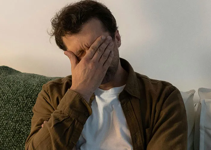 Man with hand covering face appearing regretful, illustrating the impact of wild and embarrassing drinking stories.