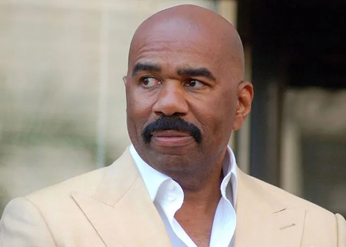 Steve Harvey dressed in a beige suit and white shirt, known for being a total gentleman in celebrity encounters.