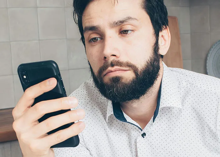 Man with beard looking at smartphone with a tired expression related to jobs that only a person without a soul would do