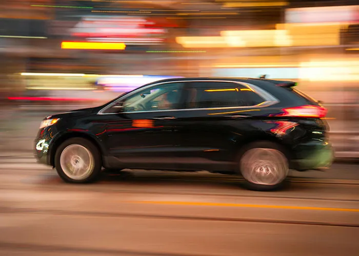 Black SUV speeding through city streets at night with blurred lights, illustrating wild and embarrassing drinking stories.