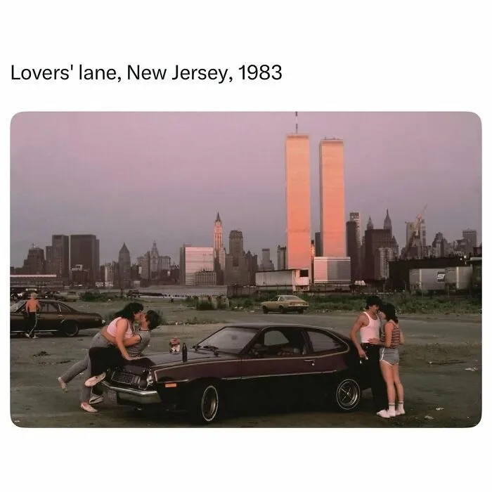 Couples kissing by a vintage car in 1983 New Jersey with Twin Towers in background, a funny meme challenging history knowledge.