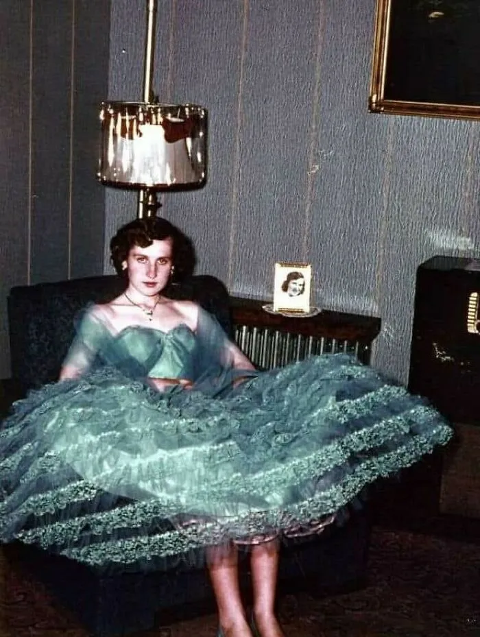 Young woman in a vintage dress sitting indoors, evoking June Cleavers vintage closet style from an old-timey era.