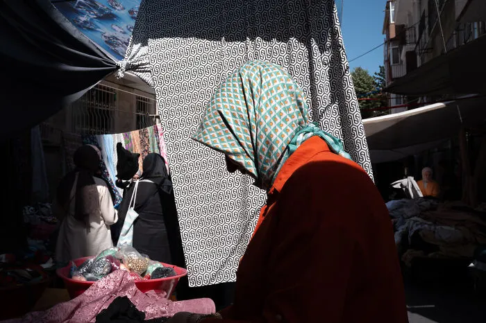 Street photographer captures a woman in a patterned headscarf shopping at an outdoor market, highlighting ordinary life moments.