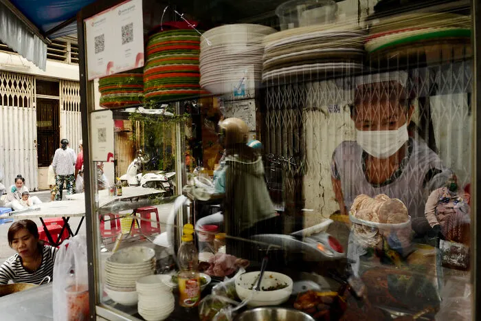 Street food vendor wearing a mask preparing food, captured in a poetic cinematic image of ordinary daily moments.