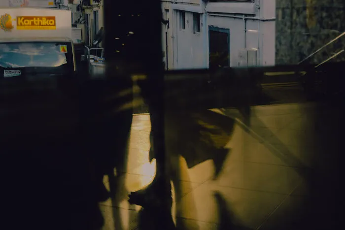 Abstract cinematic image capturing ordinary moments with shadowy reflections and soft warm lighting in an urban setting by a photographer.