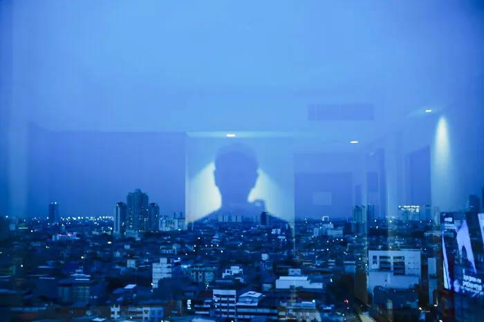 Shadowy photographer reflection over a cityscape at dusk capturing poetic cinematic moments through a window pane.