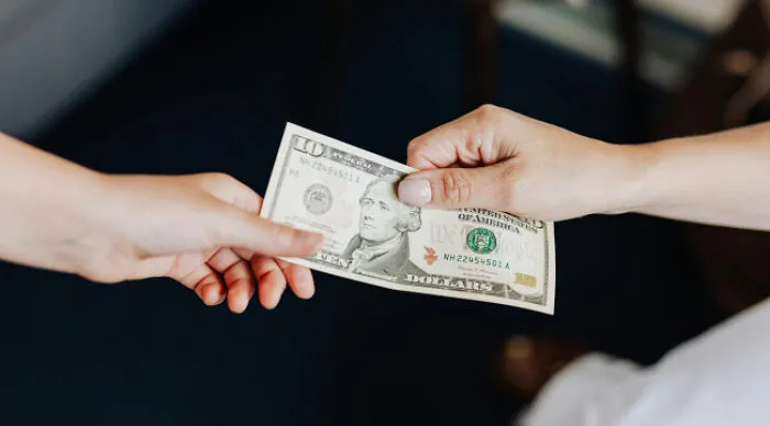 Two hands exchanging a ten dollar bill, illustrating a moral dilemma poll about am I the problem questions.