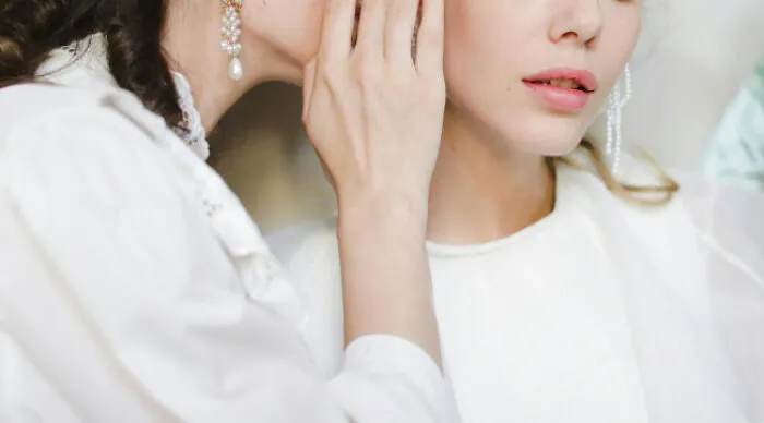 Two women in white dresses, one whispering a secret to the other, illustrating a moral dilemma poll concept.