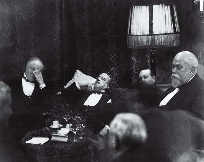 Black and white photo of men in formal wear resting and drinking, capturing an iconic moment in history.
