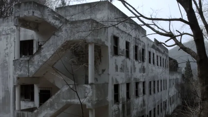 Large abandoned concrete building with peeling paint and bare trees in a gloomy setting, illustrating abandoned places.