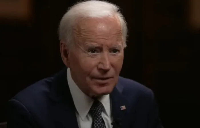 A mature man in a suit speaking during an interview about concept time facts in a dark indoor setting.