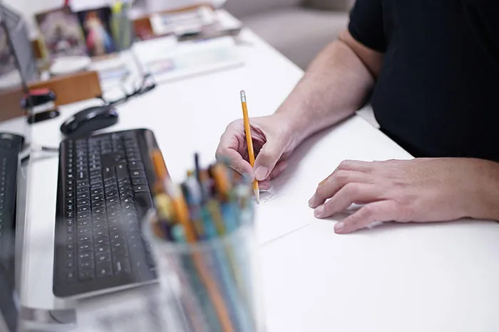 Person holding a pencil and sketching at a white desk near a keyboard, demonstrating a creative hot take concept.